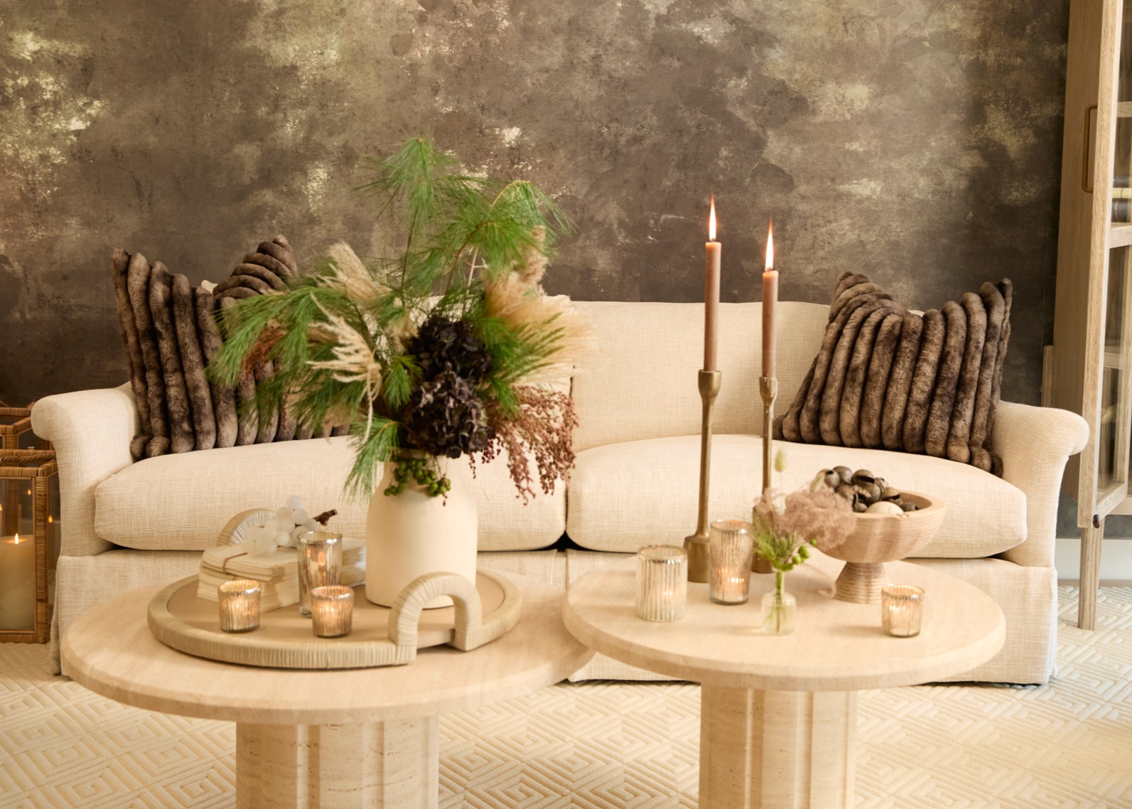 A slipcovered white sofa with faux fur pillows on top and round stone coffee tables in front