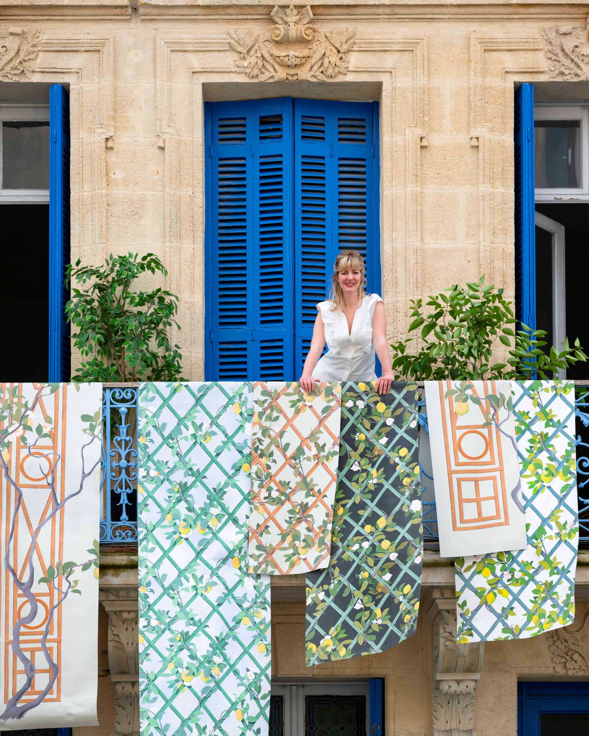 Claire Staszak of Centered by Design stands on a balcony with her Isidore Leroy Wallpaper draped over the railing