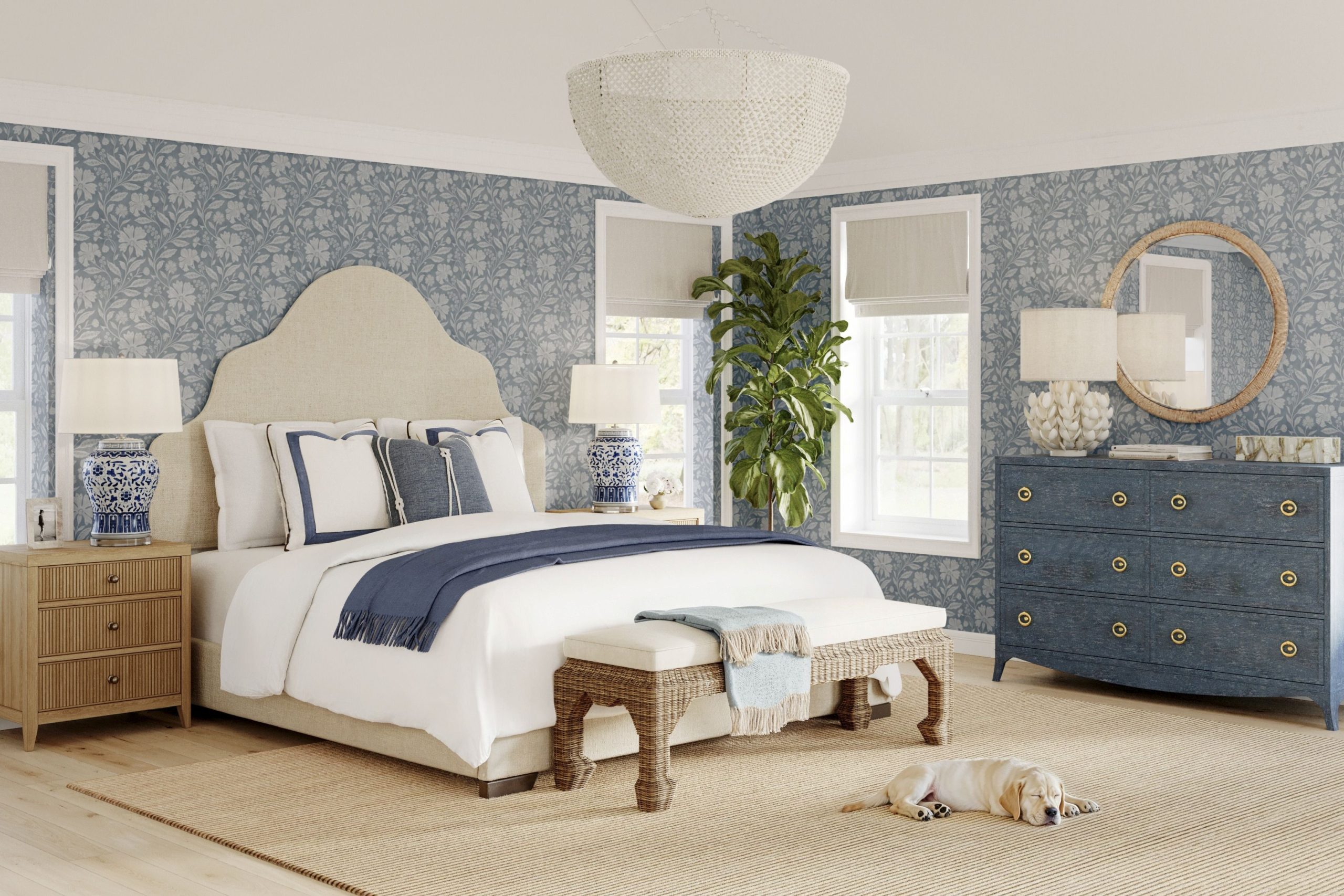 A coastal style bedroom with blue floral grasscloth wallpaper, a blue double dresser, and a king-sized bed with a curved headboard
