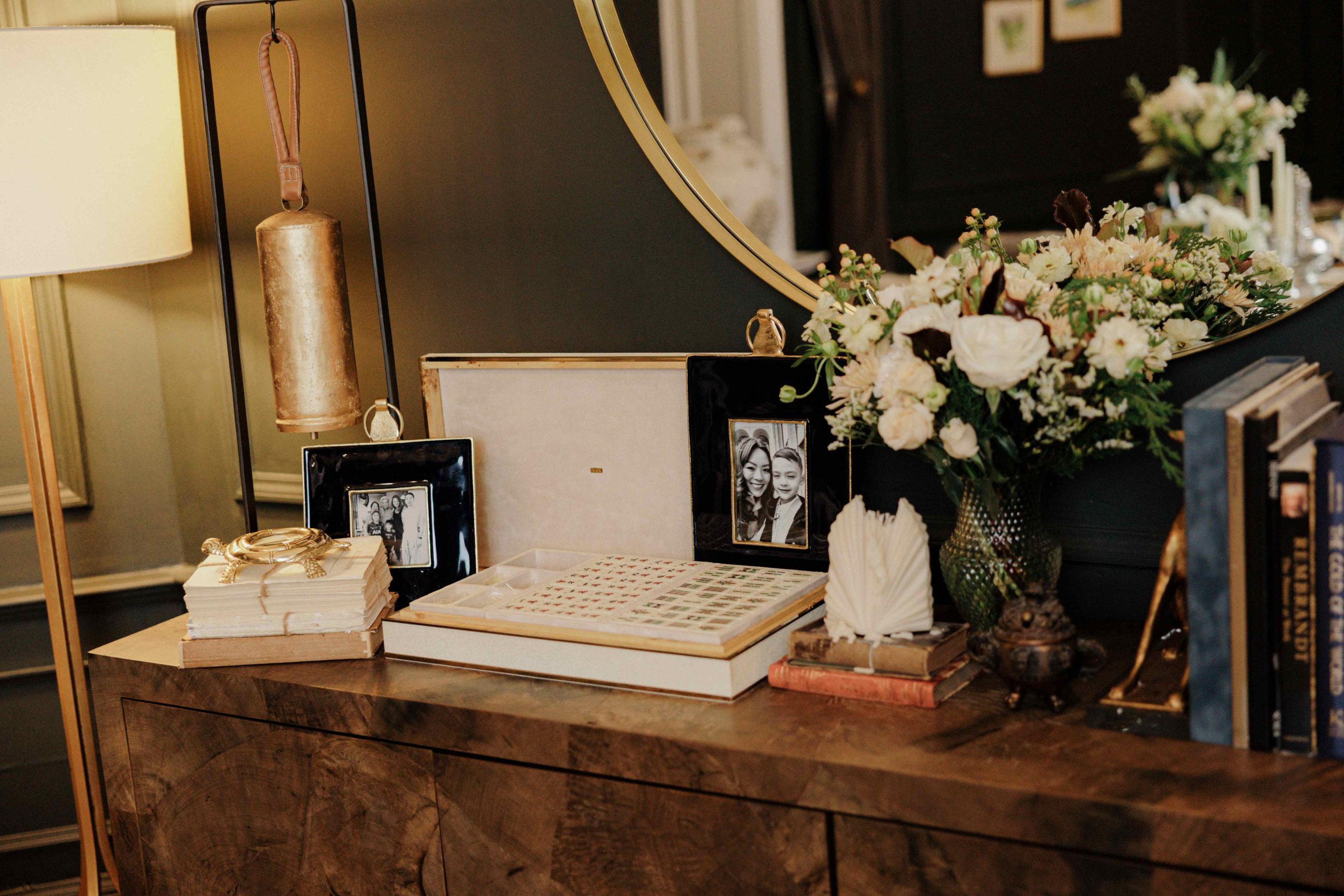A burl wood sideboard is styled in a dining room with a bouquet of flowers, board games, photo frames, and design books