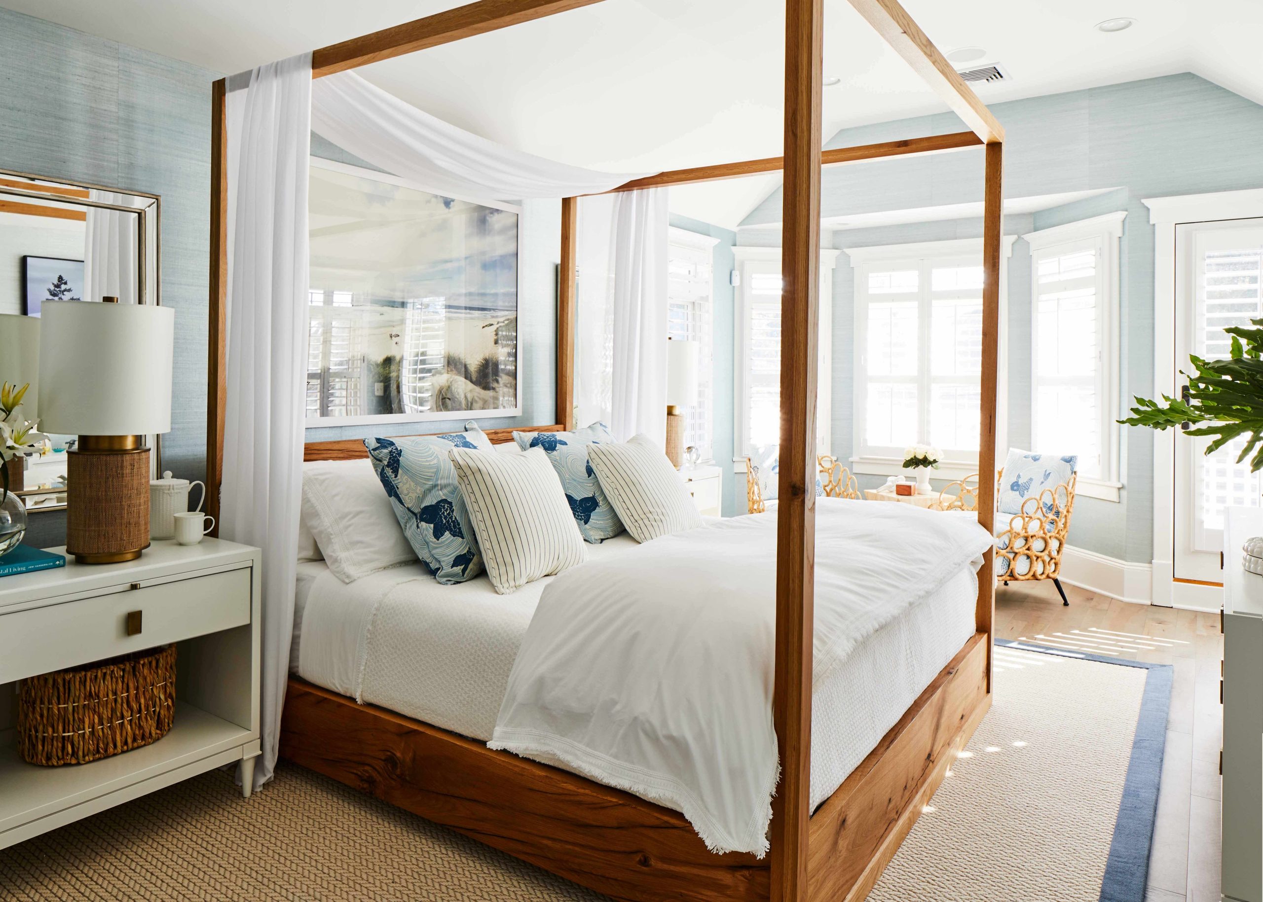 A bedroom in the Hamptons with a canopy bed, blue grasscloth wallpaper, and a natural fiber rug