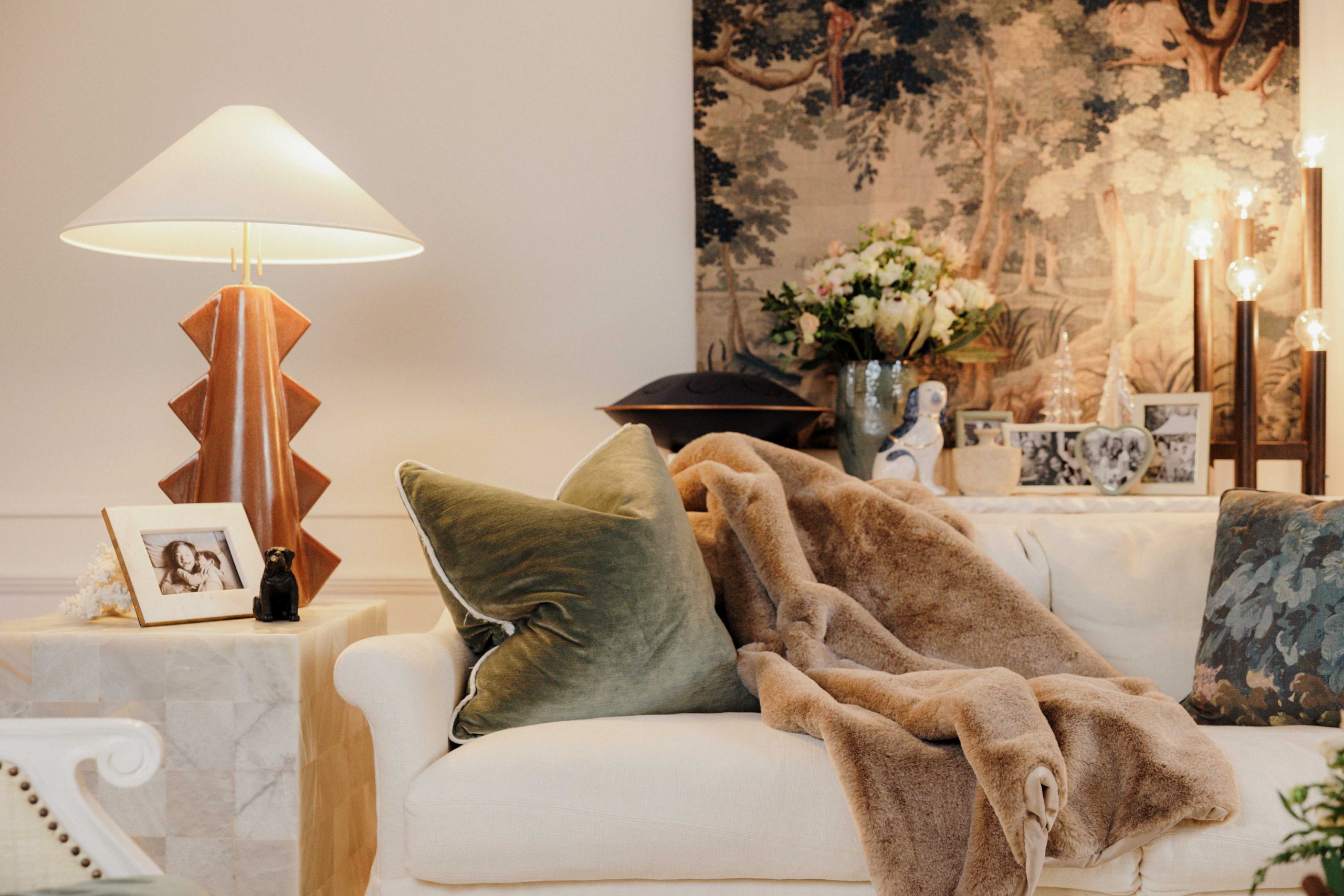 A cozy living room decorated for the holidays with soft throw blankets, plush pillows, and Simon Pierce glass Christmas trees