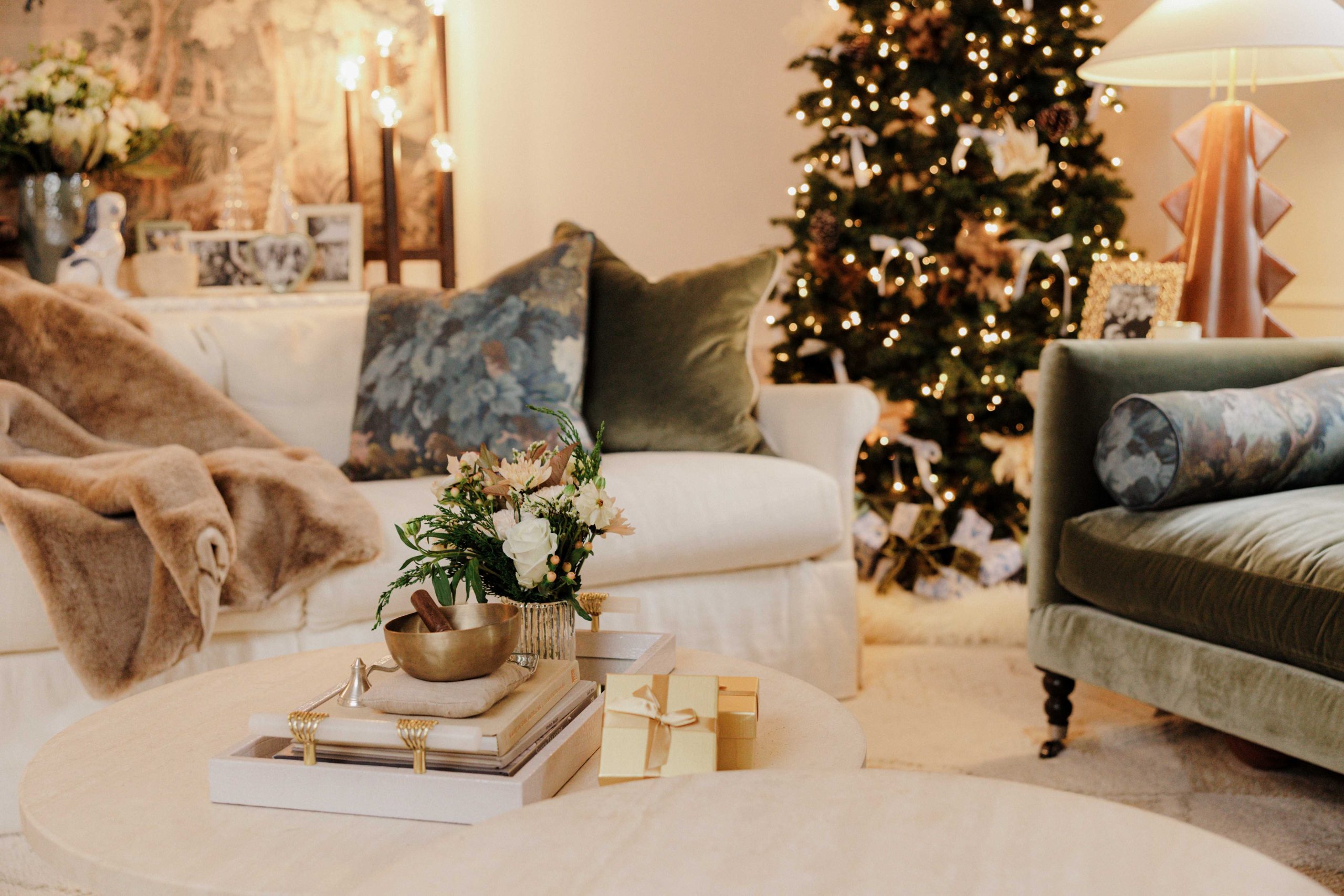 Holiday decor in an apartment living room includes a Christmas tree decorated with pampas grass, pinecones, and velvet bows, cozy blankets, and plush throw pillows