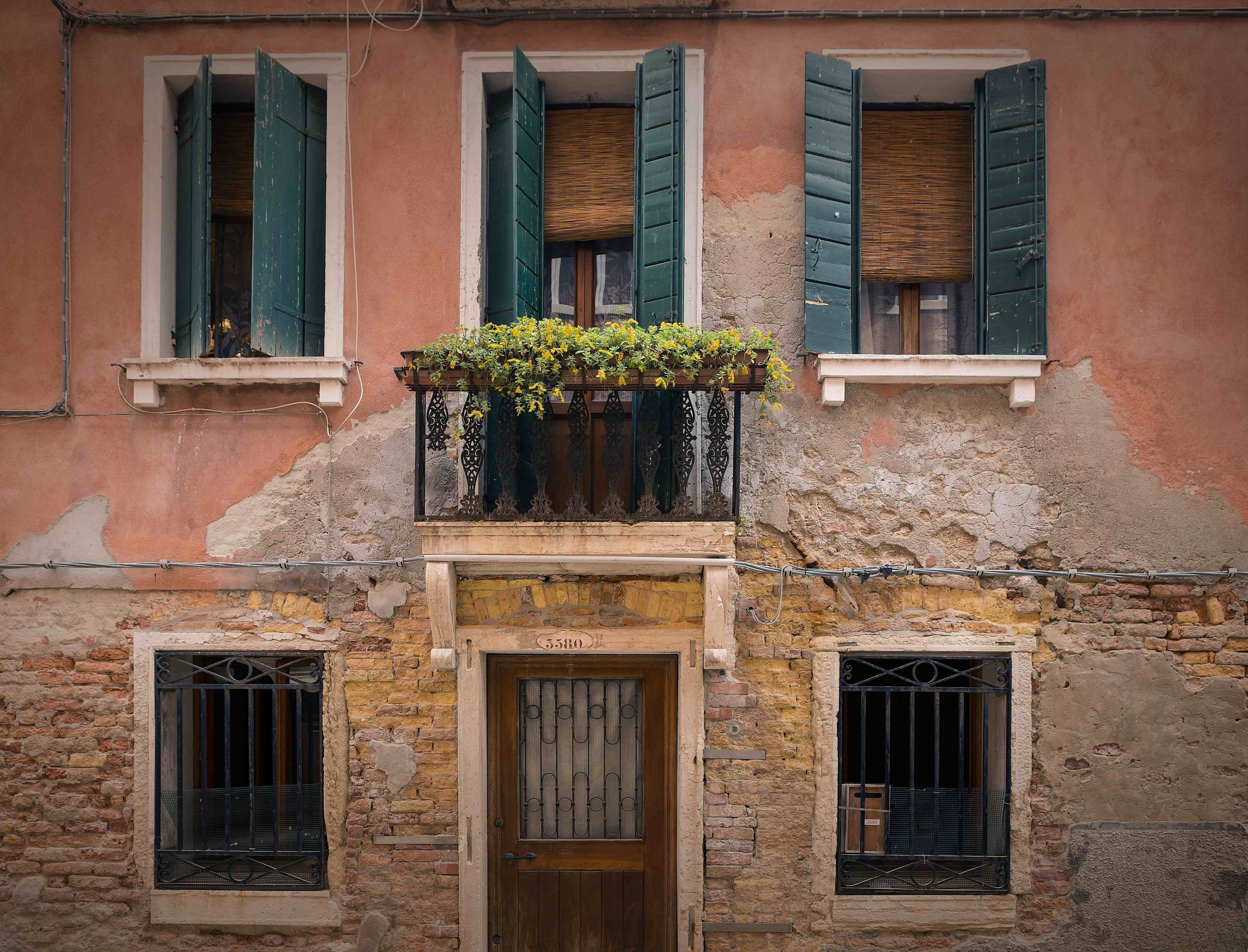 Italian building facade with plaster walls, green shutters, and a small balcony above the front door