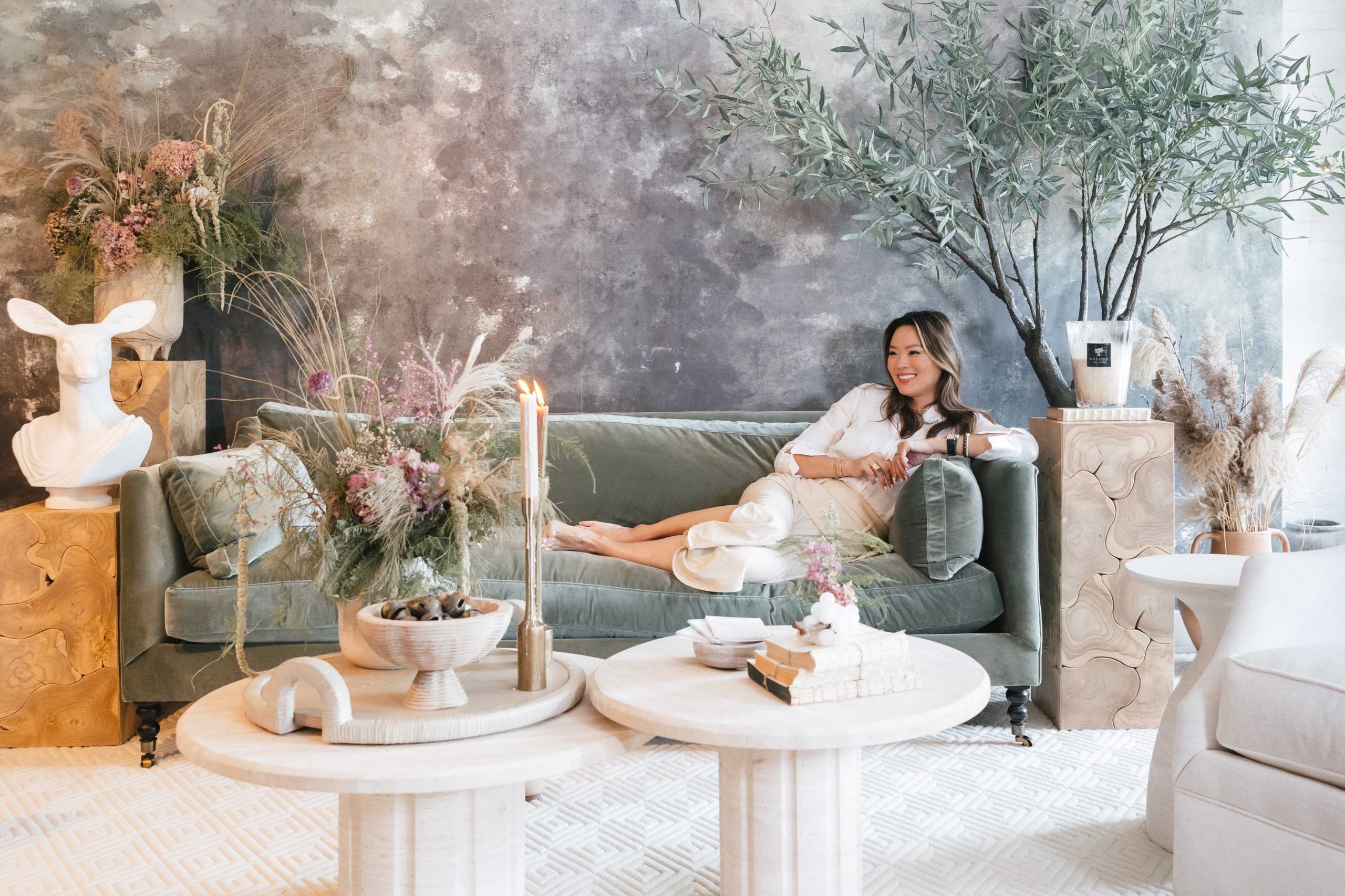 Kathy Kuo sitting on a green velvet Madeline sofa in the Kathy Kuo Home Design Showroom in Tribeca