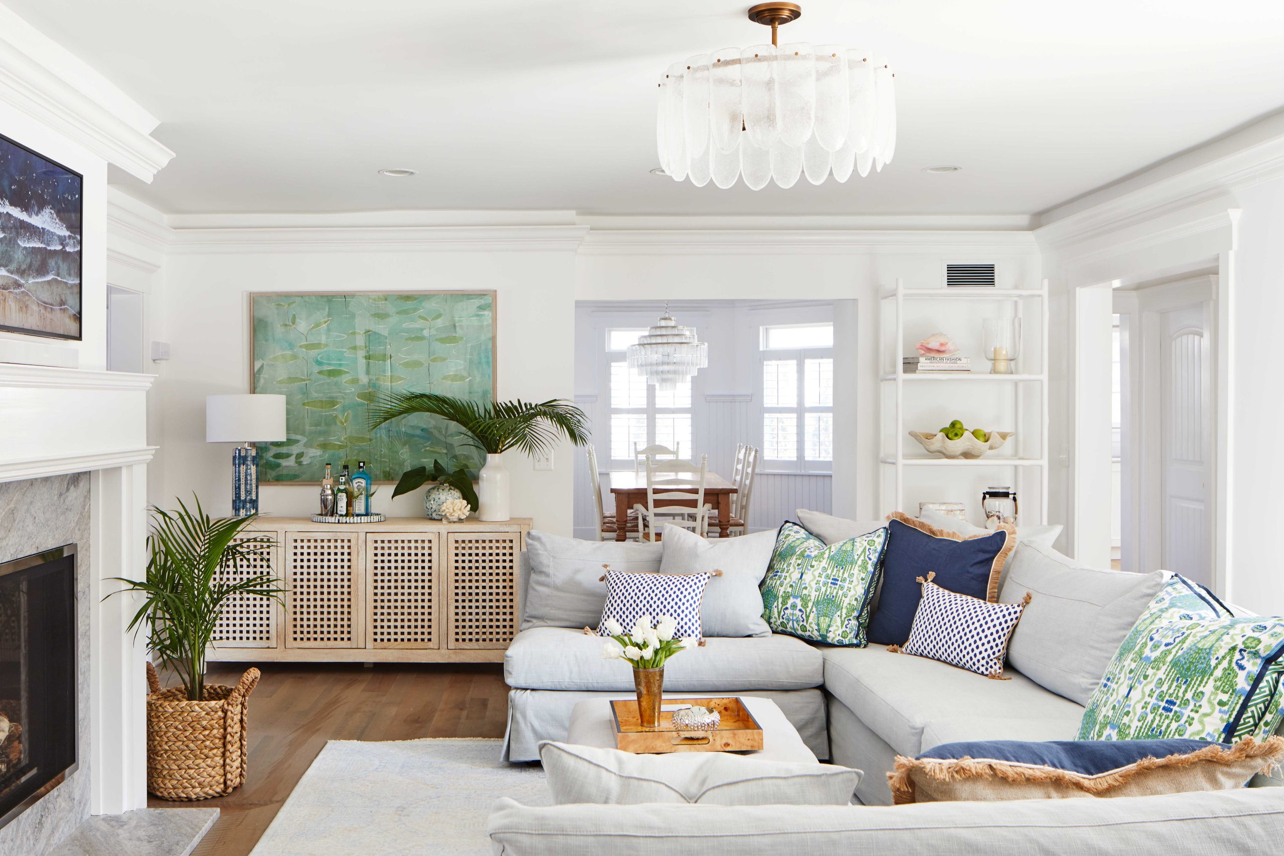 a coastal style living room with a blue and green color palette includes a light grey slipcovered sectional from Cisco, statement wall art, and a whitewashed wood sideboard