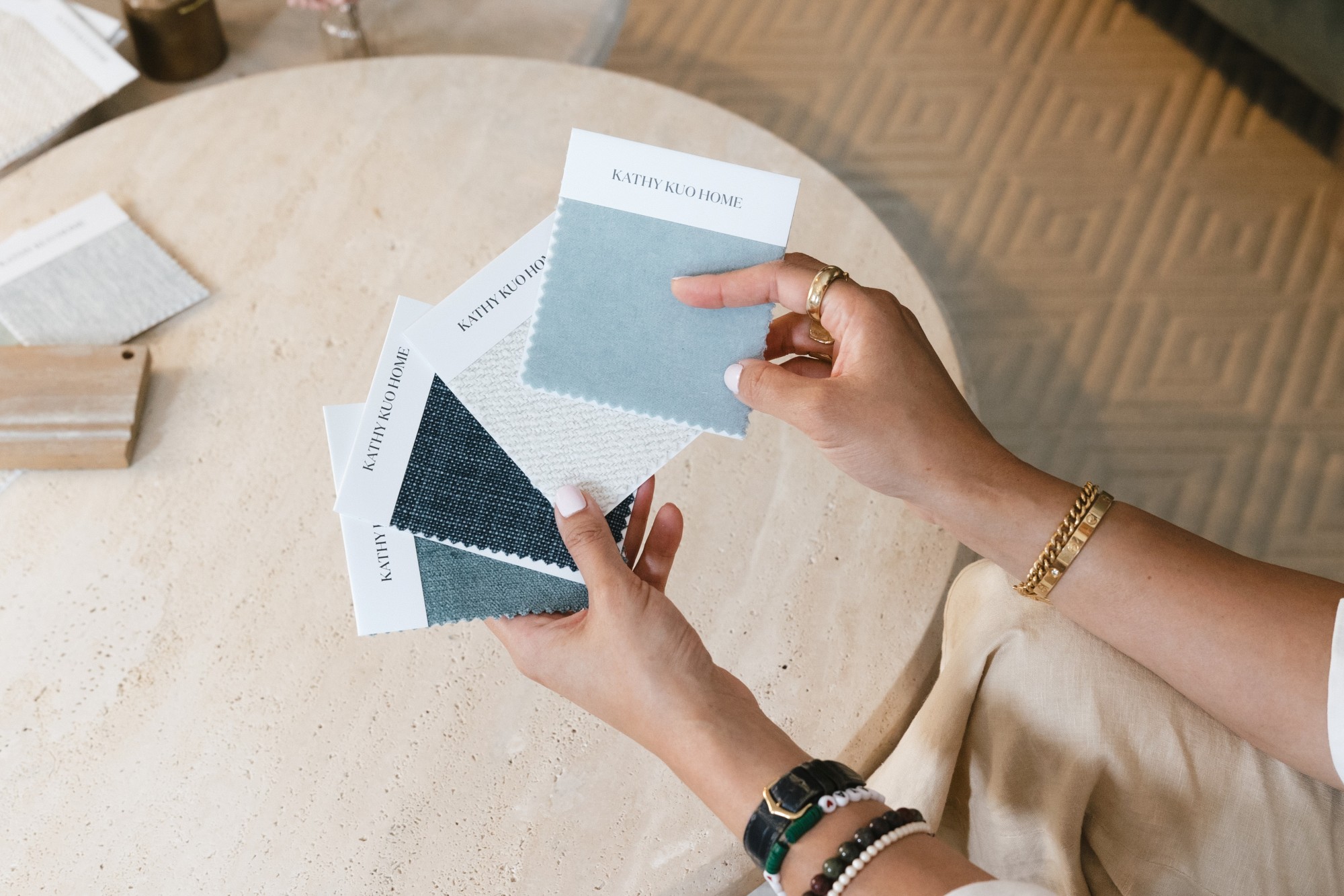Hands hold fabric swatches from Kathy Kuo Home above a stone coffee table