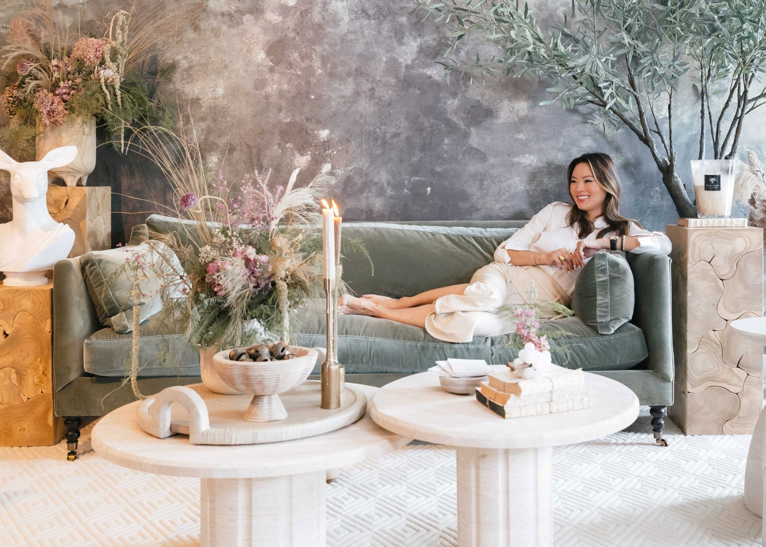Kathy Kuo sits on a green velvet sofa with turned wood legs in her New York City Design Showroom