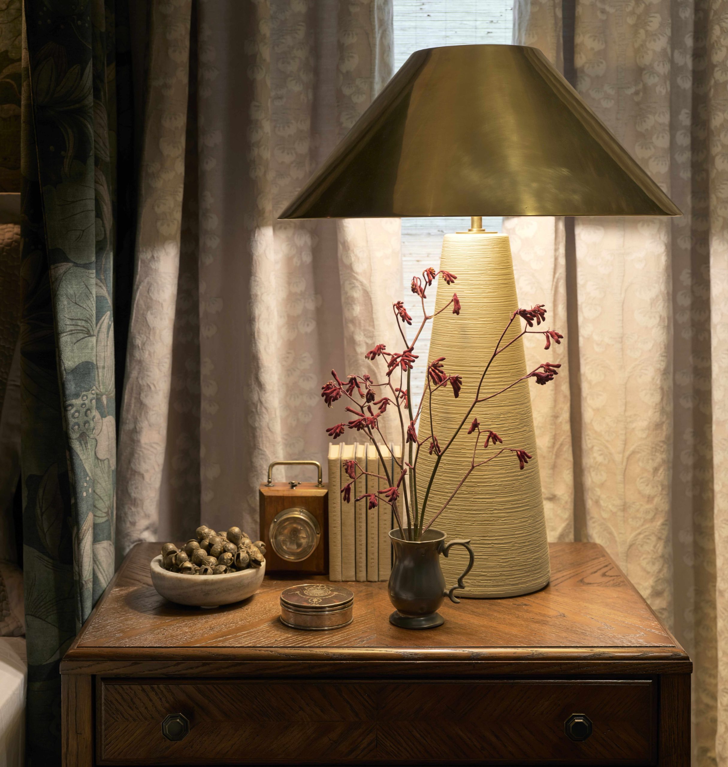 A ceramic and brass table lamp sits on top of a brown wood nightstand