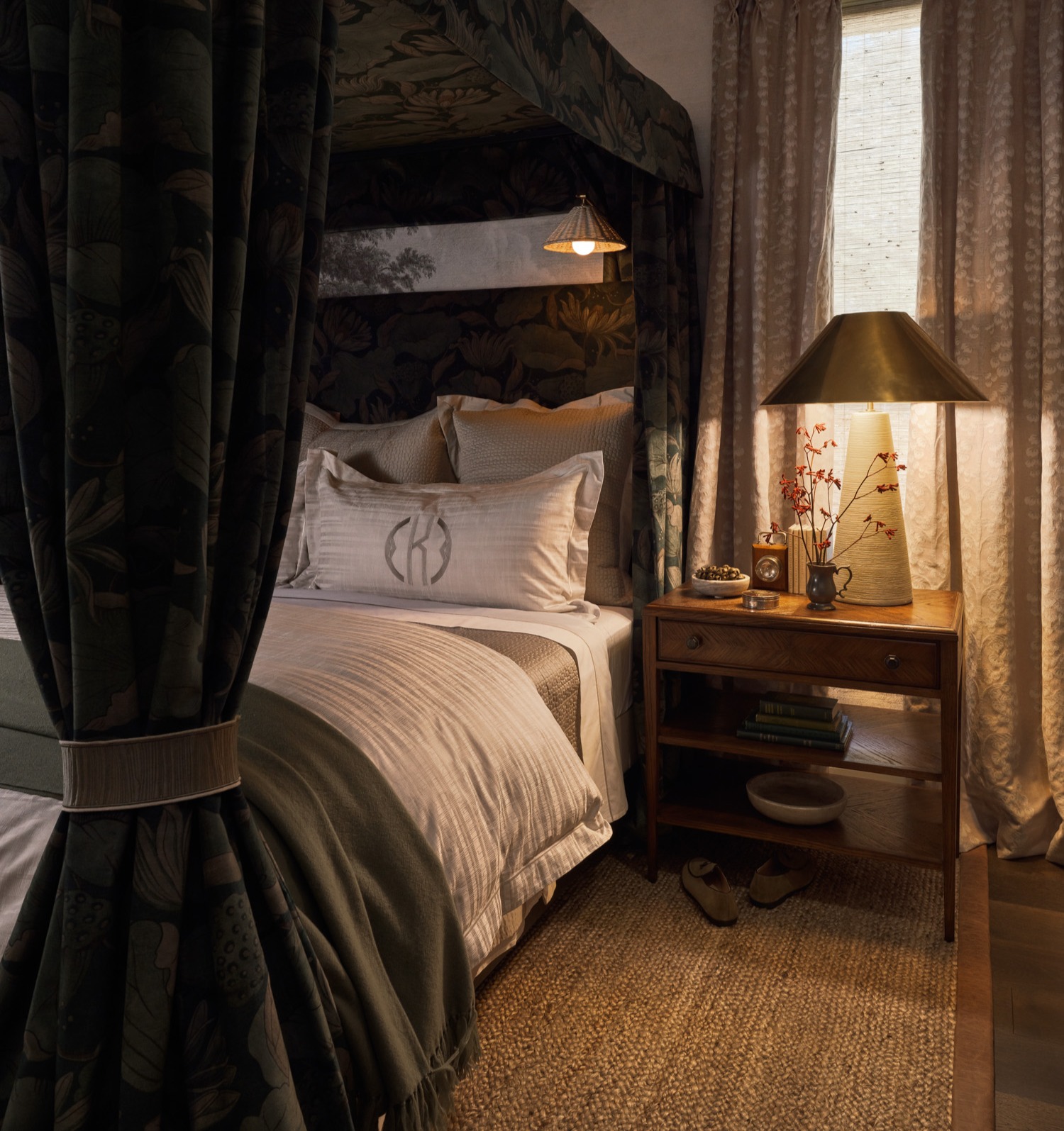 A brown wood nightstand next to a canopy bed in a cozy bedroom with a hand-braided jute rug