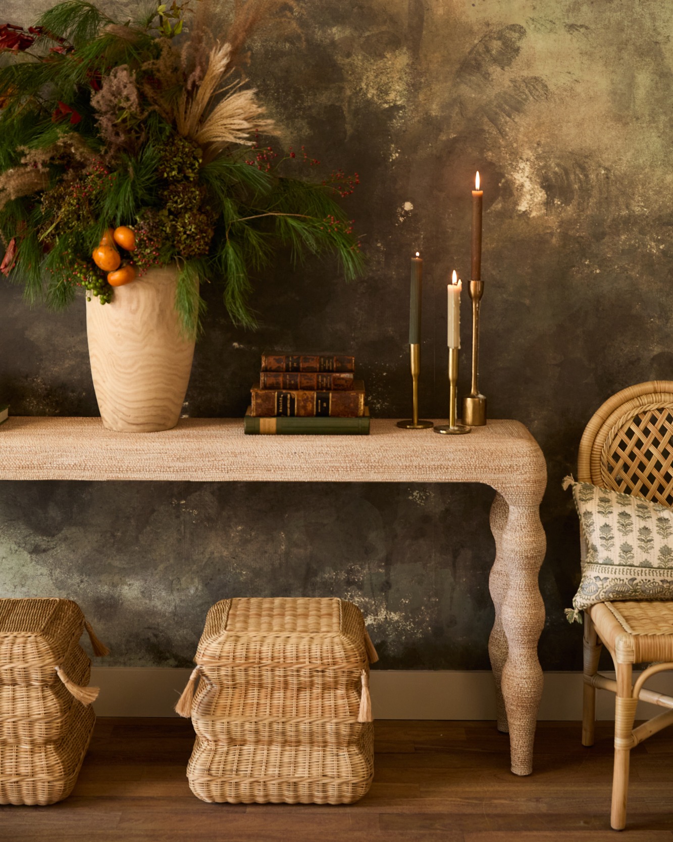 a raffia console table with turned legs has a large vase and lit taper candles on top
