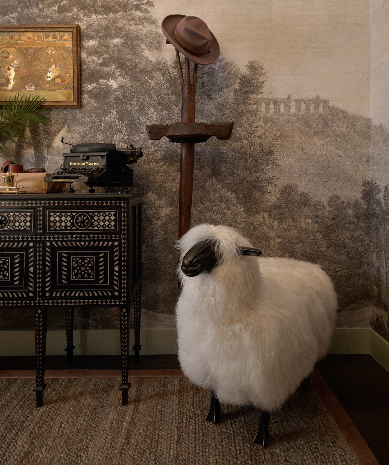 A sheep statue sits next to a teak and mother-of-pearl sideboard in a cozy bedroom