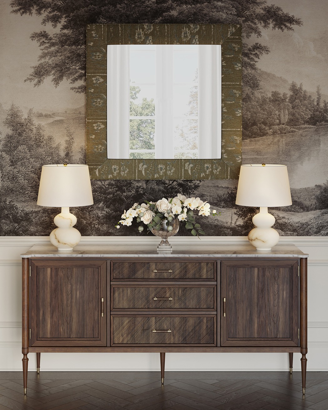 In a traditional dining room, a wood and marble sideboard is topped with two alabaster table lamps and a floral arrangement, with a square upholstered mirror above it