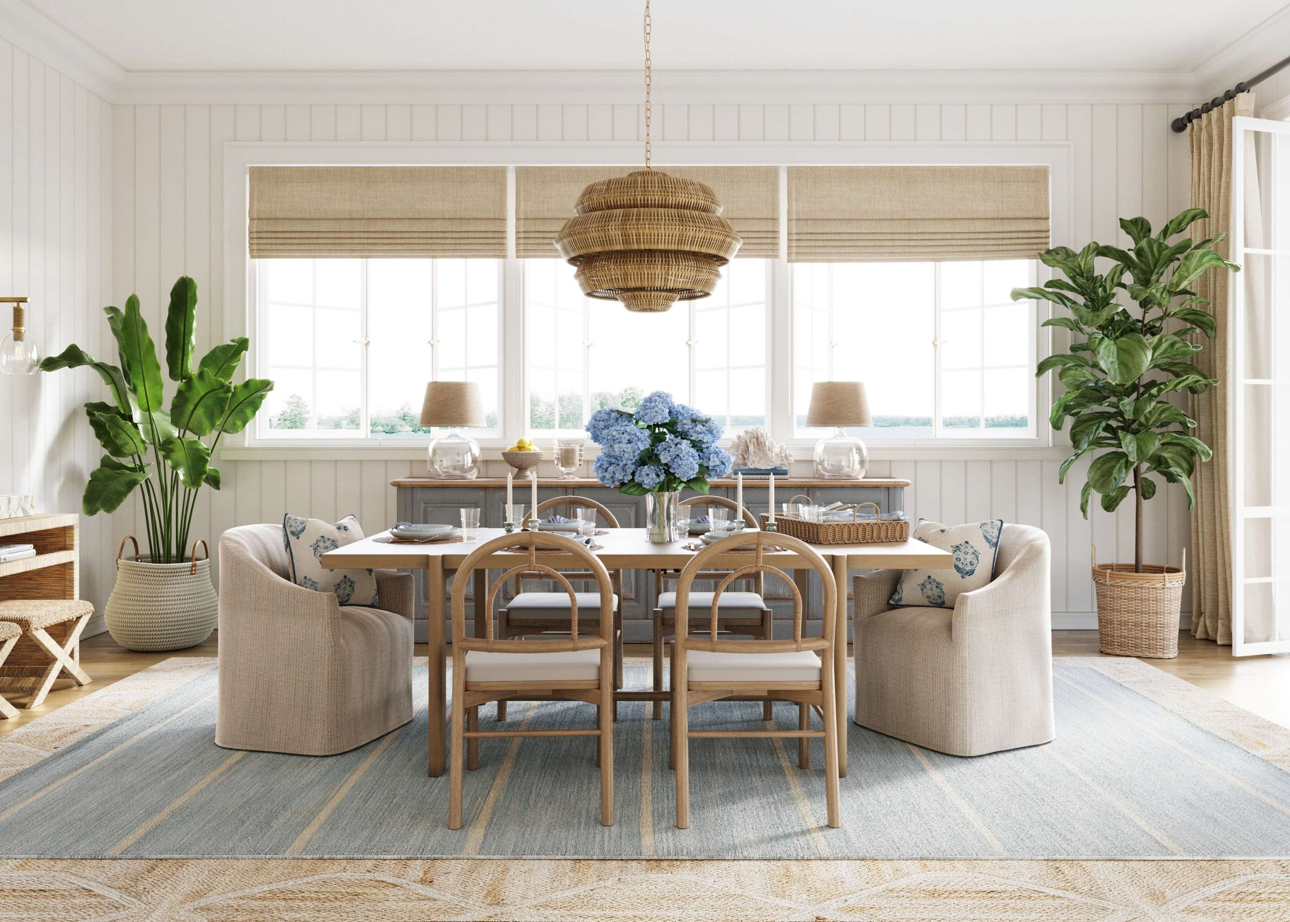 In a coastal dining room with a blue and green color palette, layered rugs sit under an oak dining table with slipcovered hostess chairs and oak dining chairs wrapped with cane