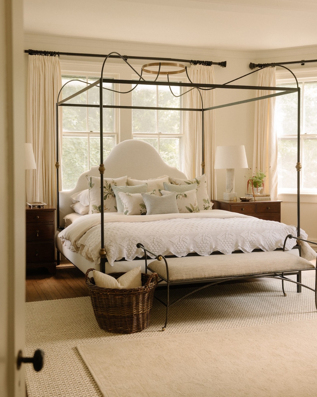 Metal canopy bed in an elegant neutral bedroom with layered rugs and an upholstered bench