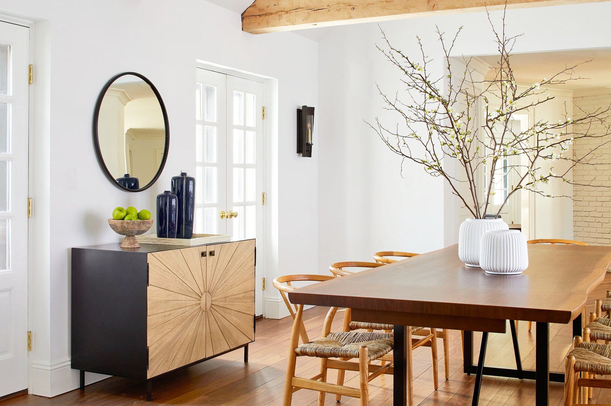 a modern farmhouse dining room with wishbone chairs and a black sideboard with sunburst doors