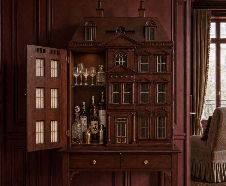 Dollhouse-style wood bar cabinet with glassware in a burgundy paneled room