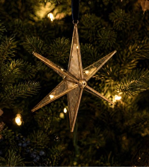 Glass star ornament hanging on a lit tree
